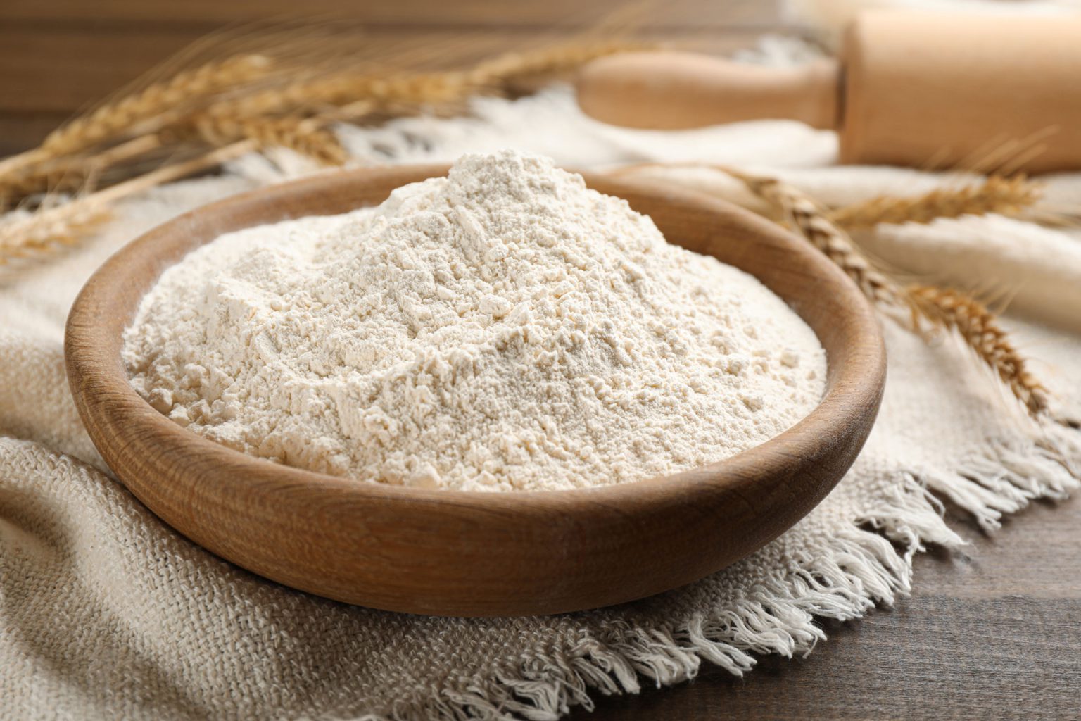 bowl with wheat flour on wooden table closeup